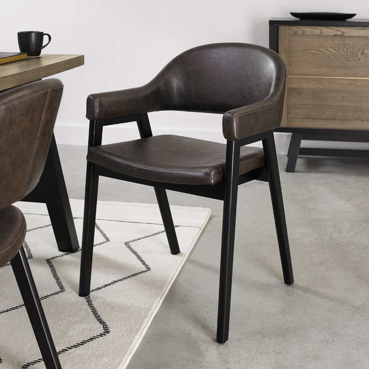 Vintage brown leather Bentley Designs dining arm chair with black legs, showing detailed upholstery and stylish wooden frame.