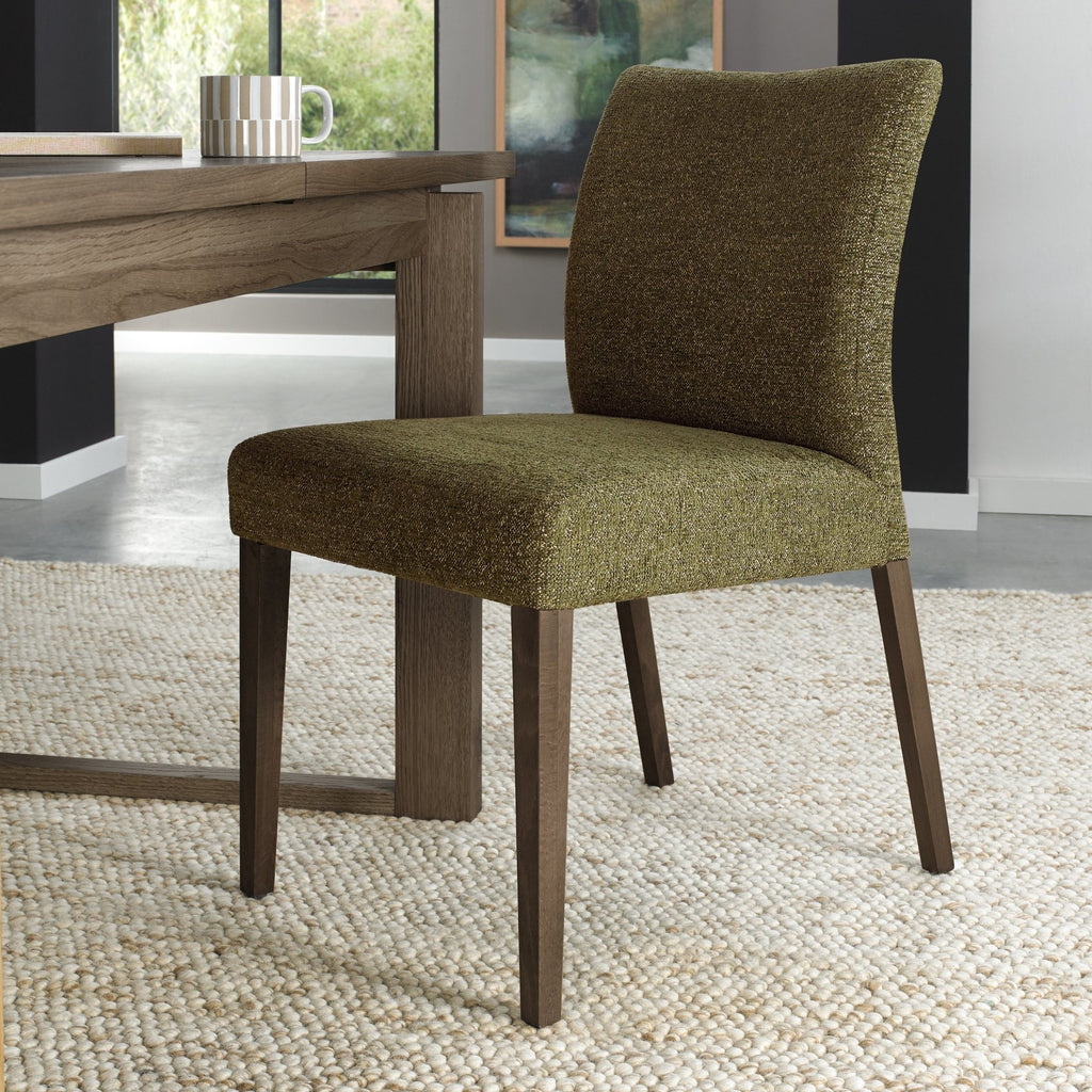 Pair of green fabric dining chairs with dark oak legs from Bentley Designs, showing the upholstered seats and sleek wooden legs.