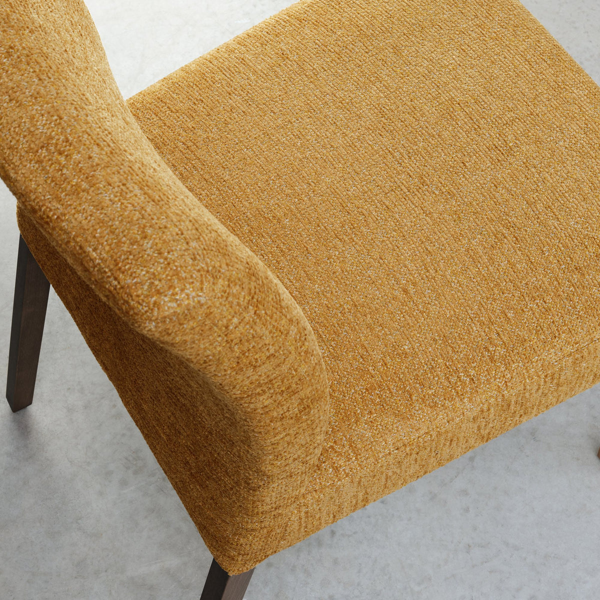 Pair of mustard yellow fabric dining chairs with dark oak legs by Bentley Designs, showing a close-up of the upholstered seats and wooden legs.