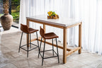 Wooden bar table with two stools in a bright room with white curtains.